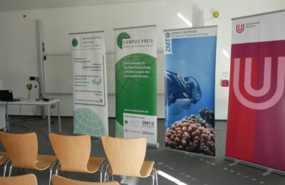 Hier sieht man einen Veranstaltungsraum, in dem Banner von der Universität Bremen, dem ZMT, der Kellner&Stoll Stiftung und des Campuspreises stehen