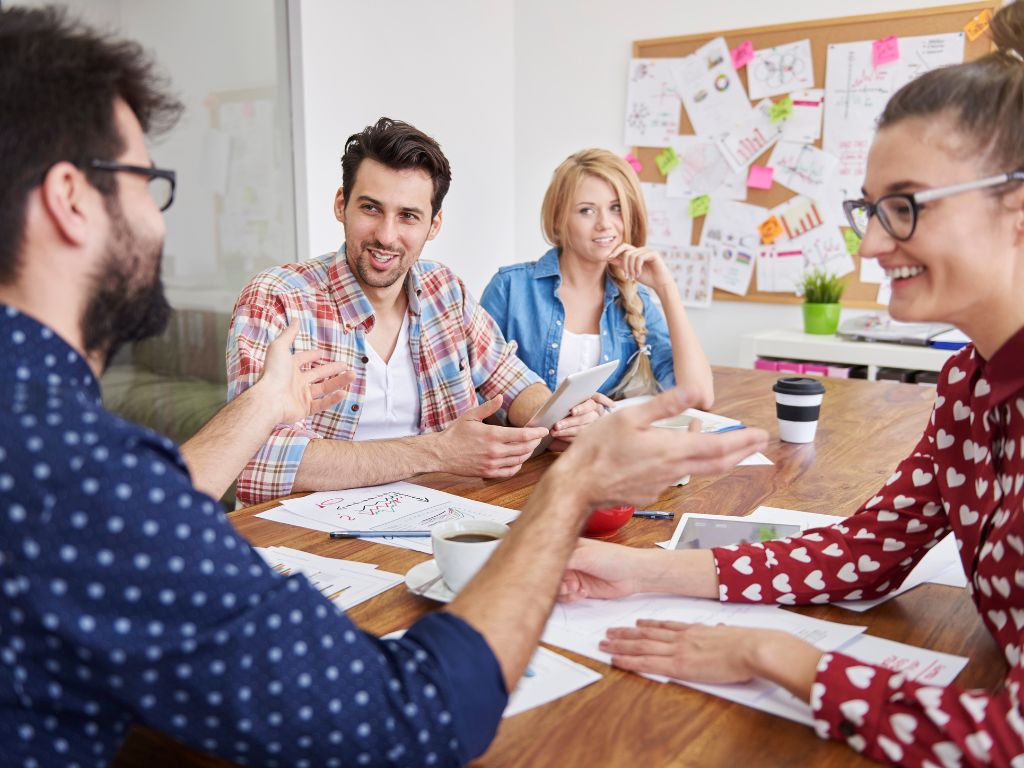 Zwei Frauen und zwei Männer sitzen an einem Holztisch und diskutieren. Im Hintergrund ist eine Pinnwann mit vielen Zetteln.