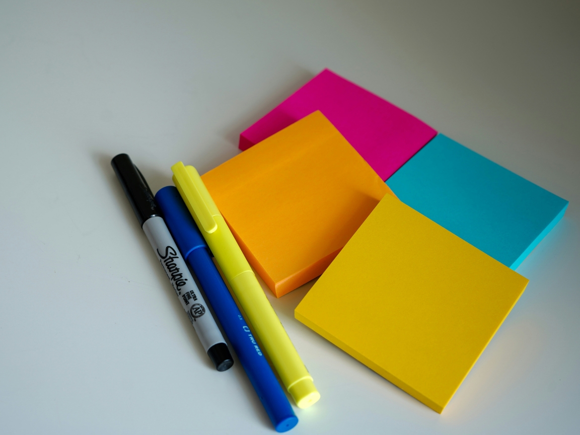 Auf dem Bild sind bunte Post-It-Blöcke und Stift zu sehen.